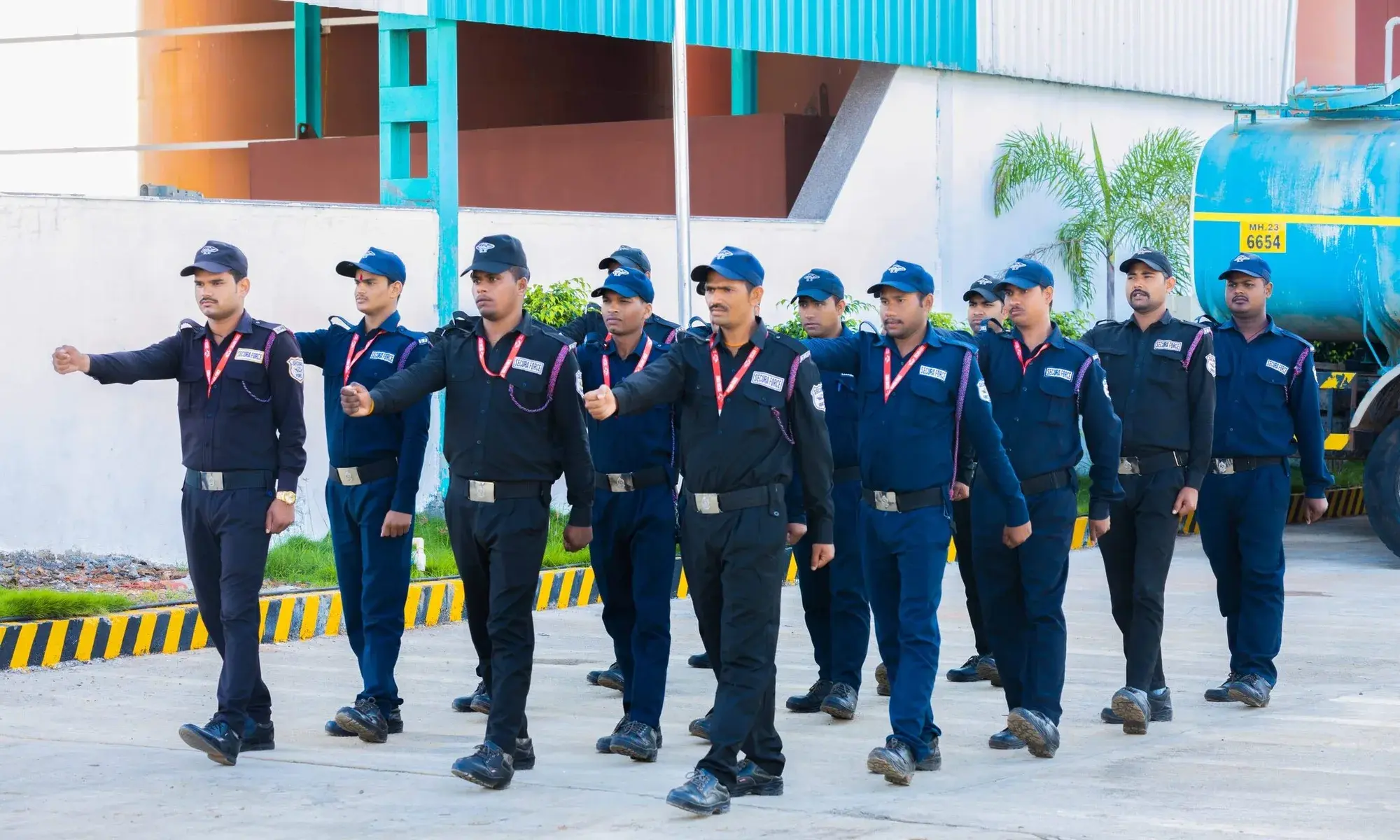 A squad of uniformed security guards marching in step across an industrial site.